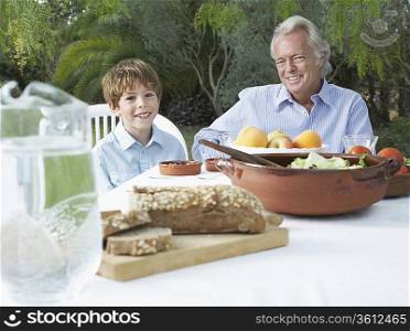 Grandfather and grandson (5-6) at garden table, portrait