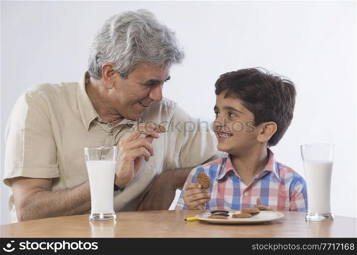 Grandfather and grandson eating biscuits with glass of milk