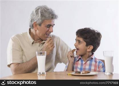Grandfather and grandson eating biscuits with glass of milk