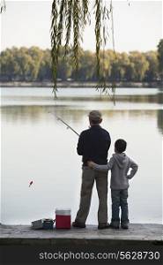 Grandfather and grandson fishing off of dock at lake