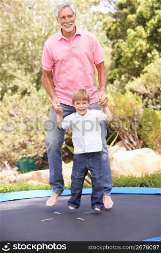 Grandfather And Grandson Jumping On Trampoline In Garden