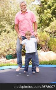 Grandfather And Grandson Jumping On Trampoline In Garden