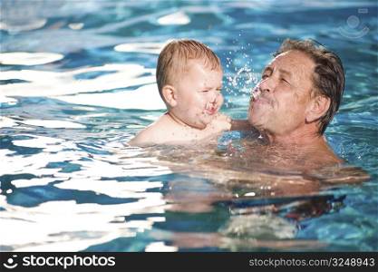 Grandfather and grandson playing together in the pool. Outdoor, summer.