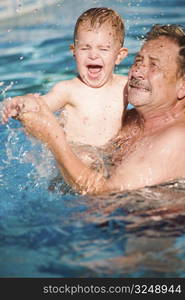 Grandfather and grandson playing together in the pool. Outdoor, summer.