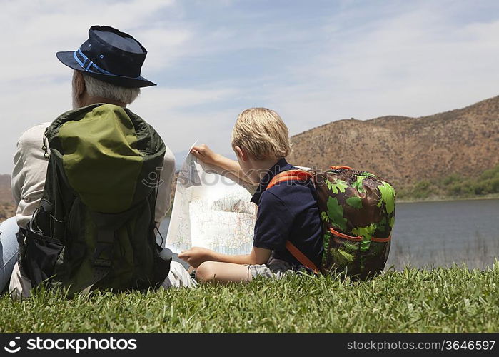 Grandfather and grandson sit with map at lakeside