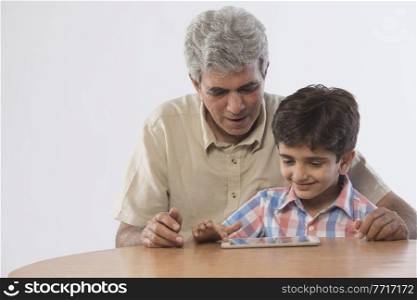 Grandfather and grandson sitting together using digital tablet