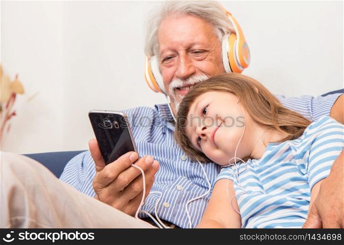 grandfather and grandson with headphones listen to music hugging each other on the couch