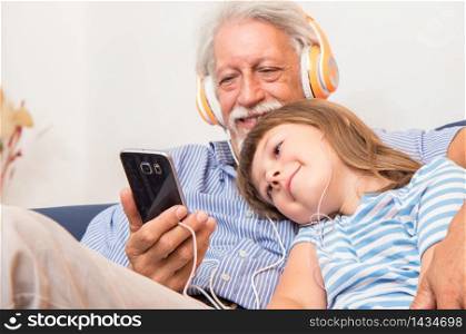 grandfather and grandson with headphones listen to music hugging each other on the couch