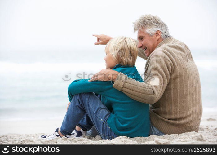 Grandfather And Son Sitting On Winter Beach Together