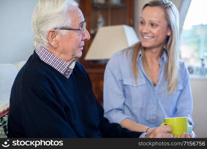 Grandfather Having Hot Drink And Talking With Adult Granddaughter At Home