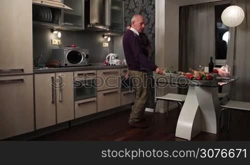 Grandfather holding toddler grandson in his arms and setting festive table with dishes while preparing to celebrate Thanksgiving together with family at home.