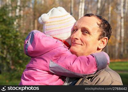Grandfather holds granddaughter on hands in wood in autumn