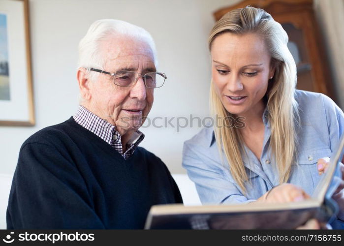 Grandfather Looking At Photo Album With Adult Granddaughter