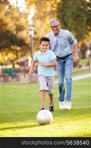 Grandfather Playing Football With Grandson In Park