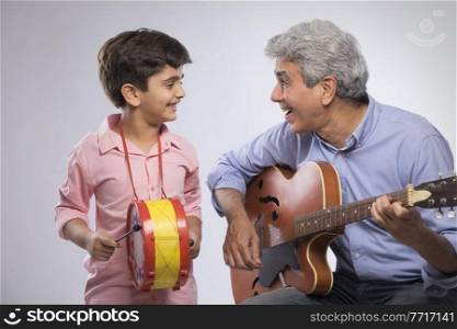 Grandfather playing guitar and grandson beating drum