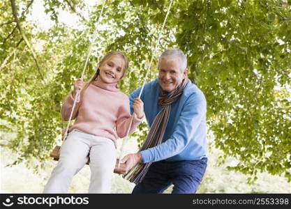 Grandfather pushing granddaughter on swing and smiling (selective focus)