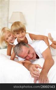 Grandfather Relaxing On Bed With Grandchildren