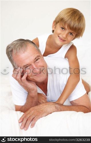 Grandfather Relaxing On Bed With Grandson
