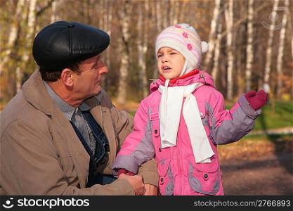 Grandfather talks with granddaughter in wood in autumn