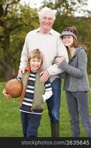 Grandfather With Grandchildren Holding Football Outside