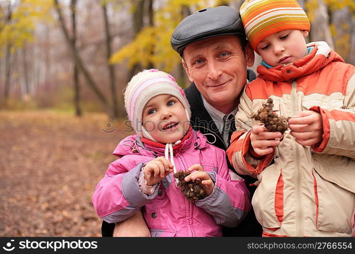 Grandfather with grandchildren in forest in autumn with burr in hands