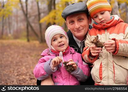 Grandfather with grandchildren in forest in autumn with burr in hands