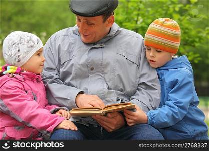 grandfather with grandchildren reads book outdoor