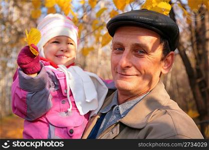 Grandfather with granddaughter on hands with yellow leafs