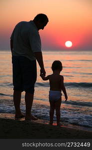 Grandfather with granddaughter on sunset at sea