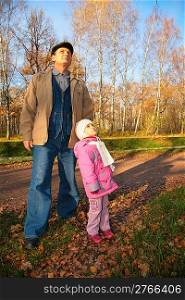 Grandfather with granddaughter stand in park in autumn and look upward