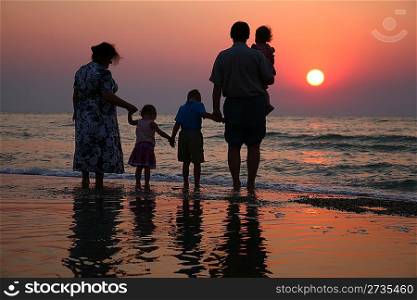 Grandfather with grandmother and the children against the background of sunset in waves