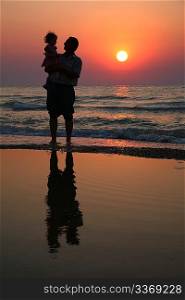 Grandfather with the child against the background of sunset at sea