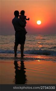 Grandfather with the child against the background of sunset at sea in water