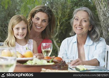 Grandma, mother and daughter (5-6) sitting at table in garden