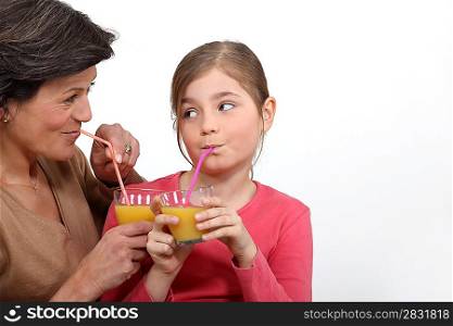 Grandmother and granddaughter drinking orange juice, studio shot