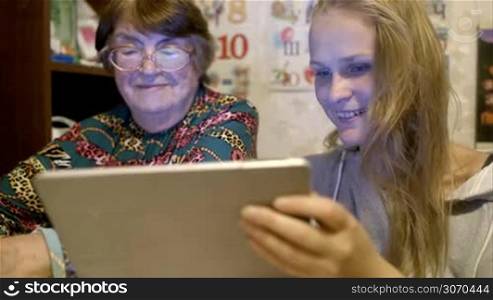 Grandmother and granddaughter looking through the photos using tablet computer. They talking and smiling