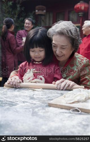 Grandmother and granddaughter making dumplings in traditional clothing