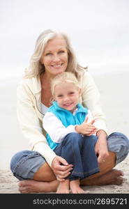 Grandmother And Granddaughter On Holiday Sitting On Winter Beach