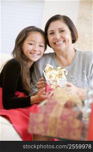 Grandmother And Granddaughter Sitting On Sofa Holding A Christmas Gift