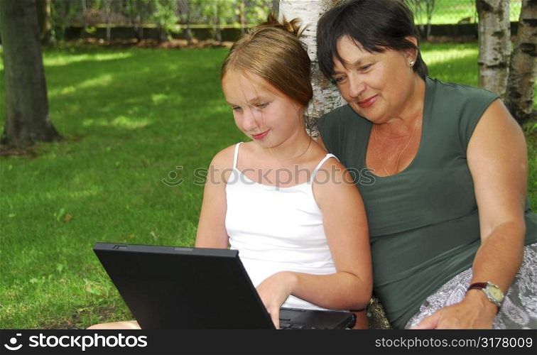 Grandmother and granddaughter sitting outside with laptop computer