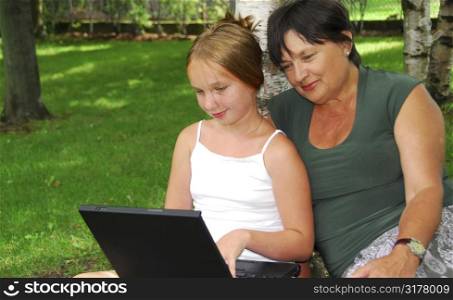 Grandmother and granddaughter sitting outside with laptop computer