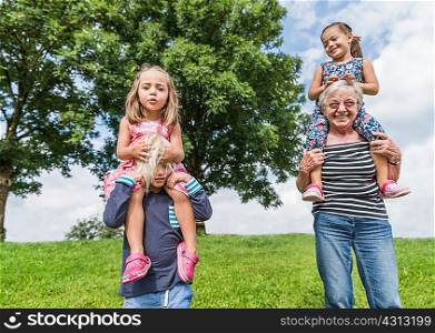 Grandmother and grandson carrying girls on shoulders, Fuessen, Bavaria, Germany