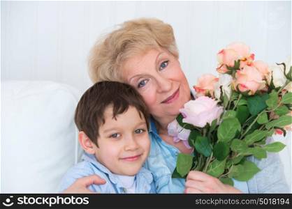 Grandmother and grandson sitting together on sofa. Granny holding flowers.
