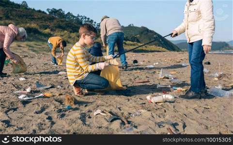 Grandmother and grandson with group of volunteers picking up trash on the beach. Volunteers cleaning the beach