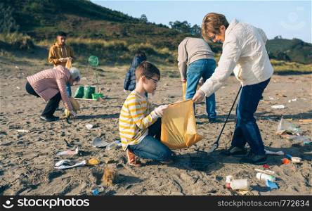 Grandmother and grandson with group of volunteers picking up trash on the beach. Volunteers cleaning the beach