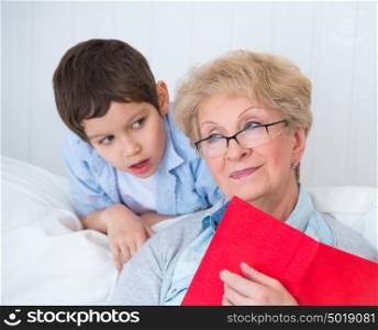 Grandmother and little boy reading book happy together at home
