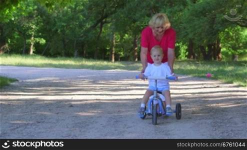Grandmother assisting child learning to ride a bicycle in the park