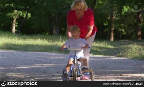 Grandmother assisting child to ride a bicycle in summer park