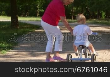 Grandmother assisting grandson to ride a bicycle in the park