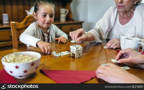 Grandmother, daughter and granddaughter playing with dominoes in the living room. Three female generations playing with dominoes